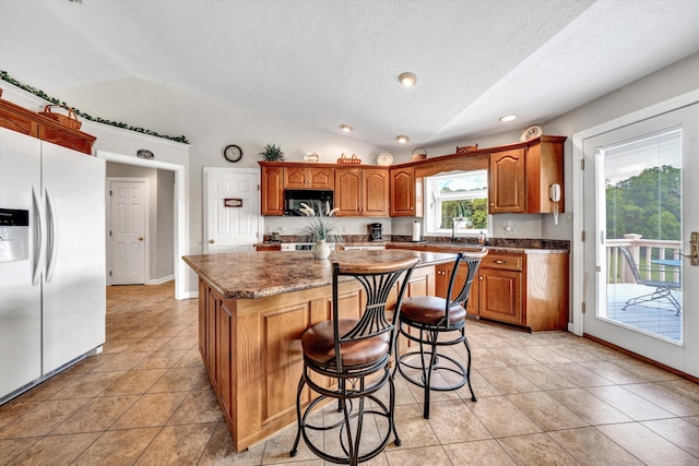 kitchen featuring light tile patterned floors, a kitchen island, vaulted ceiling, white fridge with ice dispenser, and black microwave