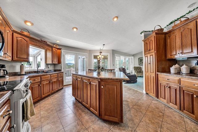 kitchen with dark countertops, stainless steel electric range oven, brown cabinets, a center island, and hanging light fixtures