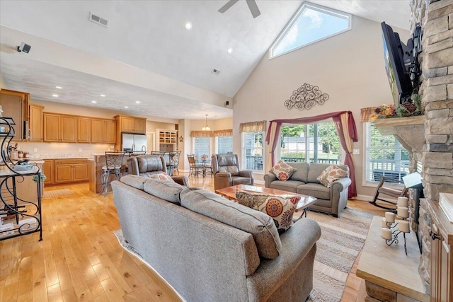 living room featuring ceiling fan, high vaulted ceiling, a fireplace, and light hardwood / wood-style floors