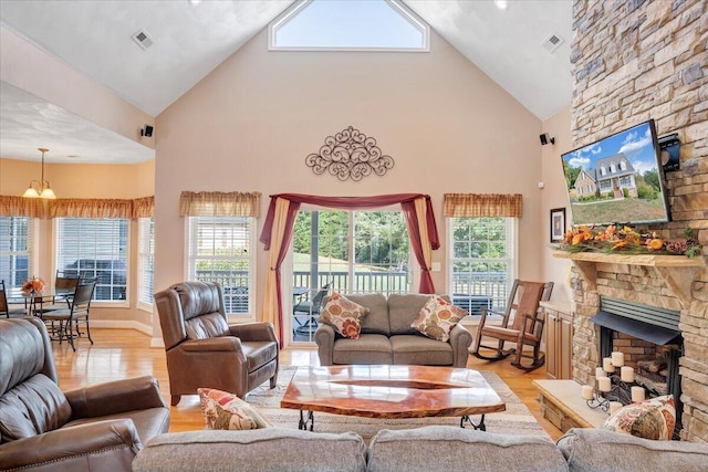 living room featuring an inviting chandelier, high vaulted ceiling, a fireplace, and light hardwood / wood-style floors