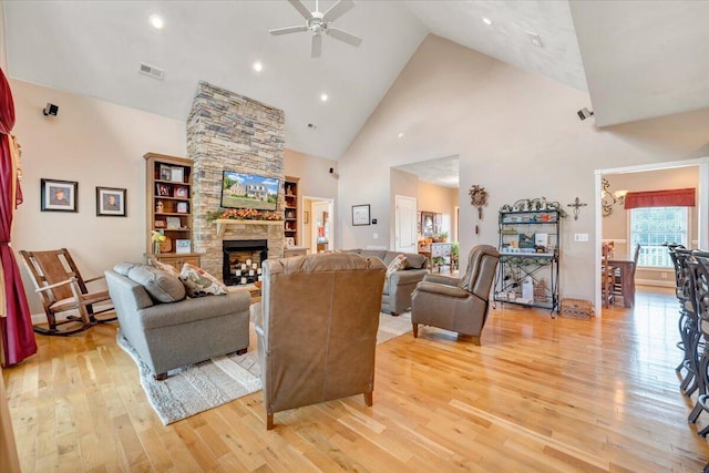 living room featuring a stone fireplace, light hardwood / wood-style flooring, high vaulted ceiling, and ceiling fan