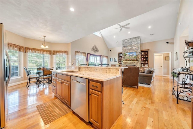 kitchen with appliances with stainless steel finishes, decorative light fixtures, sink, a center island with sink, and light wood-type flooring