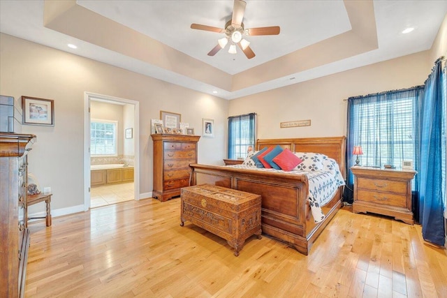 bedroom with a raised ceiling, multiple windows, and light hardwood / wood-style flooring