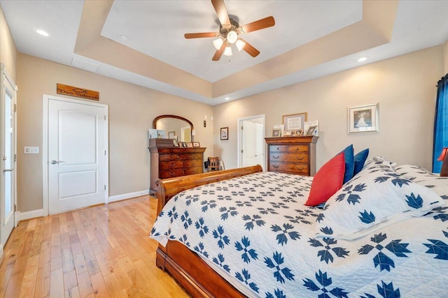 bedroom with a raised ceiling, ceiling fan, and light hardwood / wood-style floors