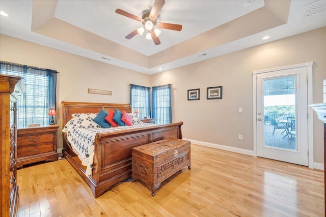 bedroom featuring multiple windows, light wood-type flooring, and a tray ceiling