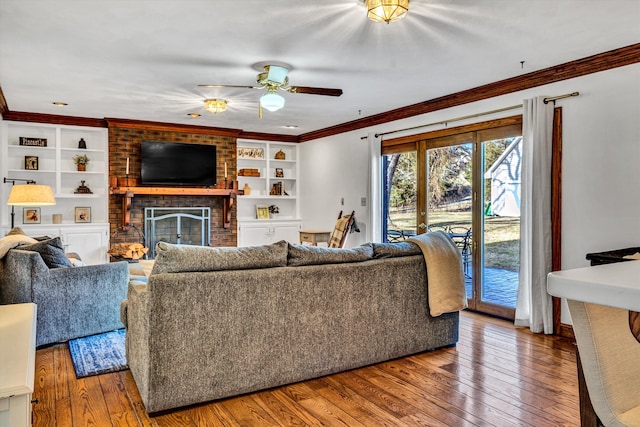 living room featuring built in shelves, a brick fireplace, ornamental molding, ceiling fan, and hardwood / wood-style floors