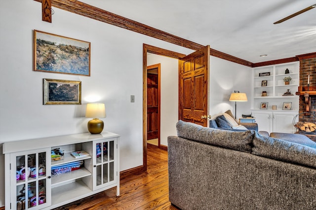 living room featuring built in shelves, crown molding, wood-type flooring, ceiling fan, and a fireplace