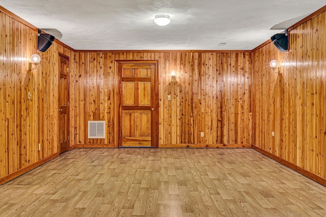 empty room featuring light hardwood / wood-style flooring, ornamental molding, and wooden walls