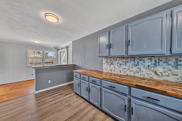 kitchen featuring tasteful backsplash, butcher block countertops, a barn door, and light wood-type flooring