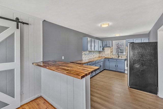 kitchen featuring stainless steel refrigerator, backsplash, wood counters, a barn door, and light wood-type flooring