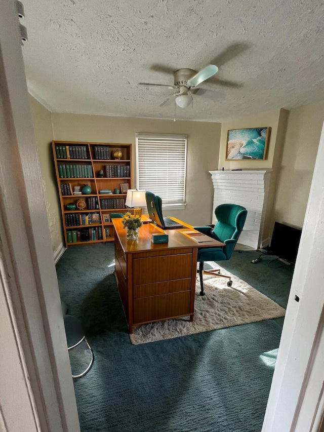 office area with ceiling fan, a fireplace, a textured ceiling, and dark colored carpet