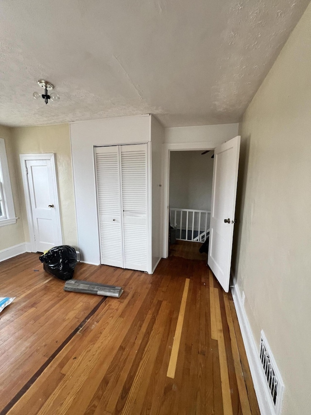 unfurnished bedroom with wood-type flooring, a textured ceiling, and a closet