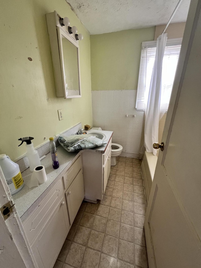 full bathroom with shower / tub combo with curtain, tile walls, vanity, a textured ceiling, and toilet