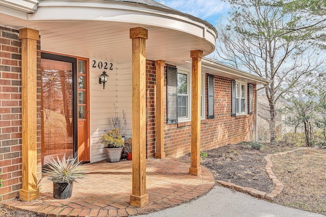 view of exterior entry with covered porch and brick siding