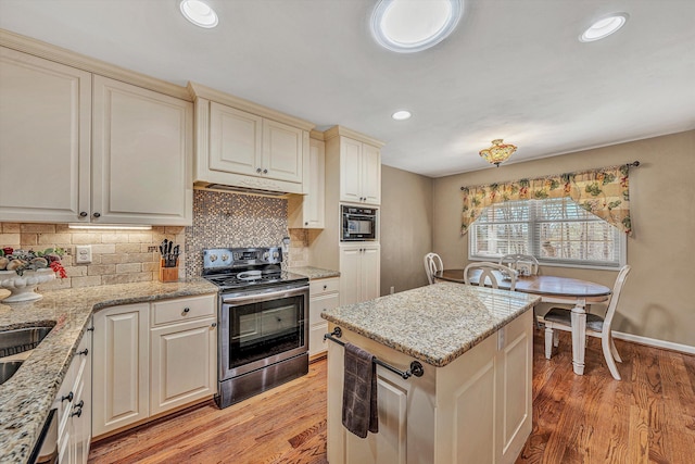 kitchen with light stone counters, decorative backsplash, stainless steel electric stove, and light wood-type flooring