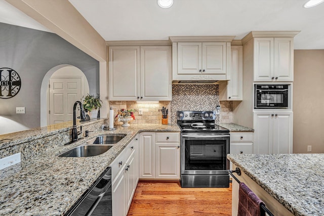 kitchen featuring sink, tasteful backsplash, black appliances, light stone countertops, and light wood-type flooring