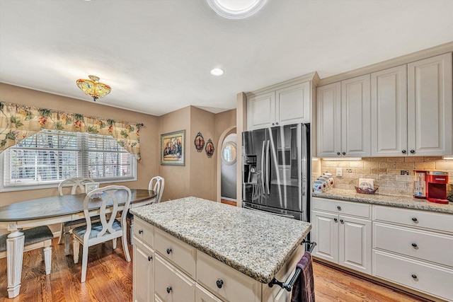 kitchen with decorative backsplash, stainless steel fridge, light stone counters, and light hardwood / wood-style flooring