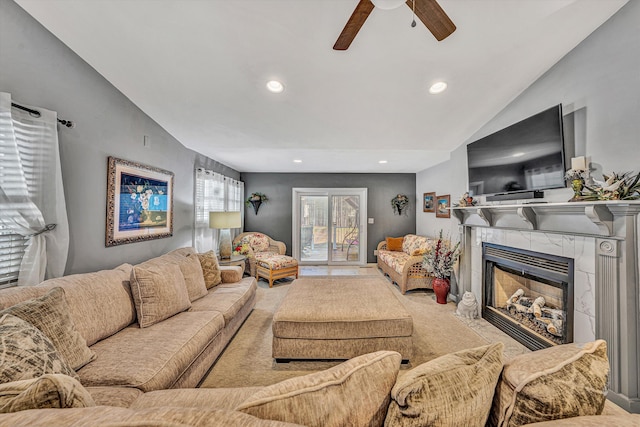 carpeted living room with ceiling fan, lofted ceiling, and a tiled fireplace