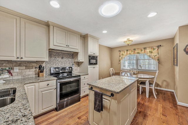 kitchen with stainless steel electric stove, a kitchen island, decorative backsplash, light hardwood / wood-style floors, and light stone countertops