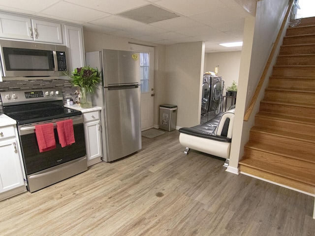 kitchen with light hardwood / wood-style flooring, independent washer and dryer, stainless steel appliances, decorative backsplash, and white cabinets