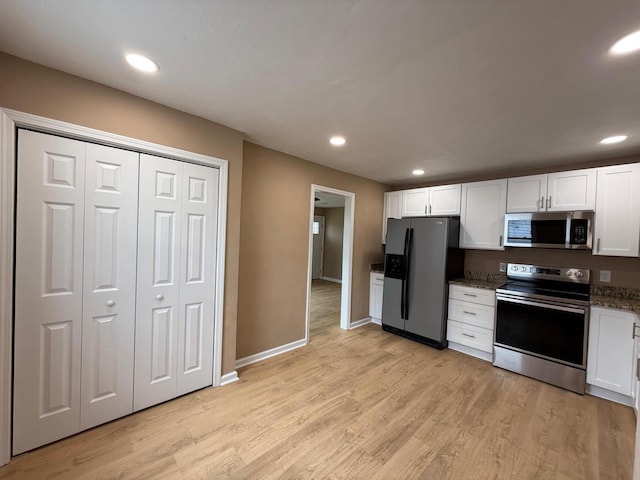 kitchen featuring dark stone countertops, stainless steel appliances, light hardwood / wood-style flooring, and white cabinets