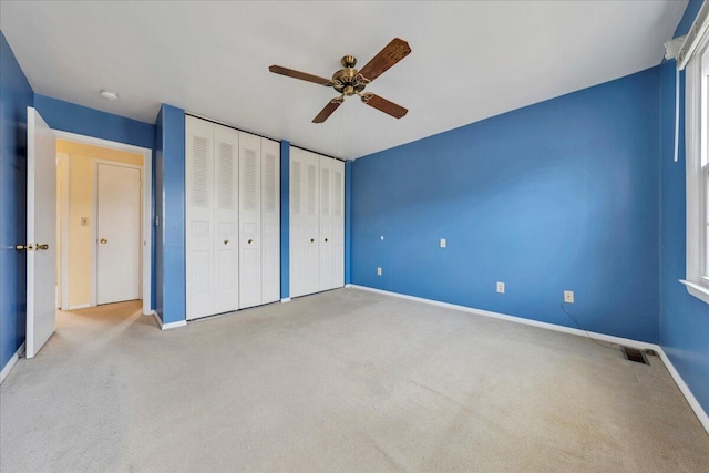 unfurnished bedroom featuring ceiling fan, light colored carpet, and two closets