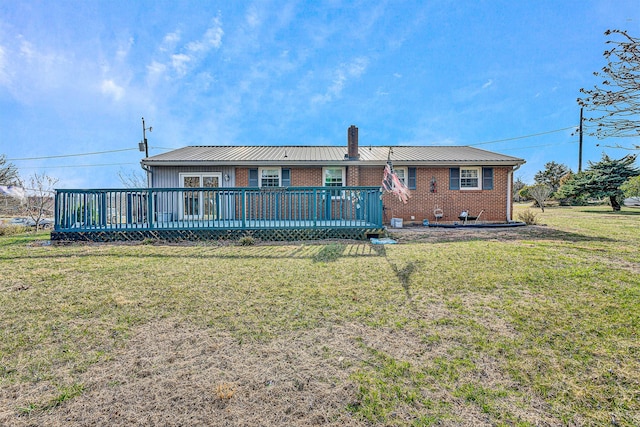 rear view of house featuring brick siding, a chimney, a deck, and a yard