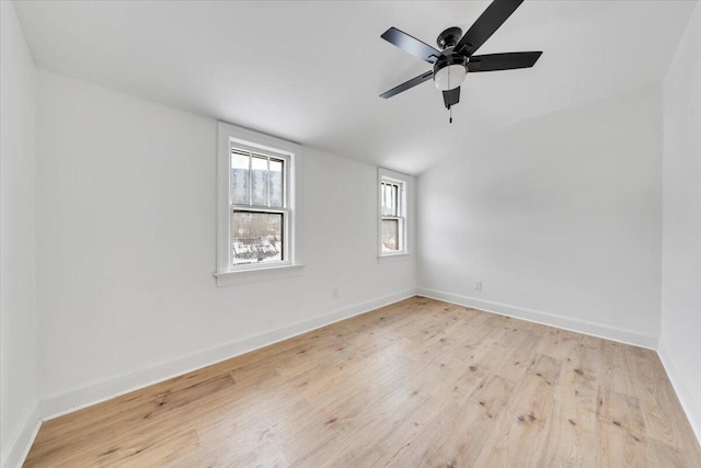 spare room featuring light wood-style flooring, baseboards, vaulted ceiling, and a ceiling fan