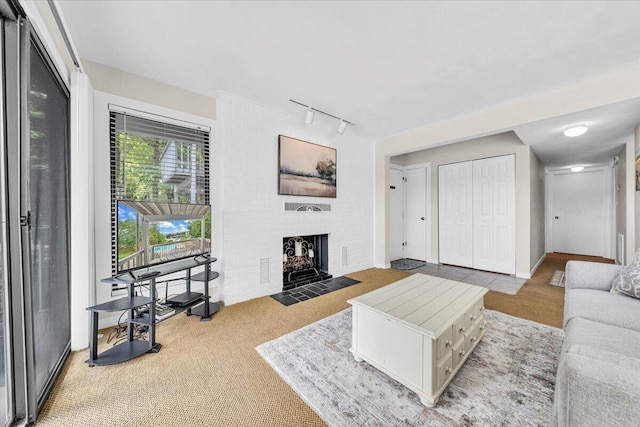 living room with a brick fireplace, rail lighting, and carpet flooring