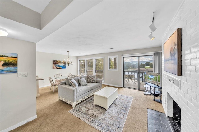 living room with a brick fireplace, a notable chandelier, track lighting, and carpet