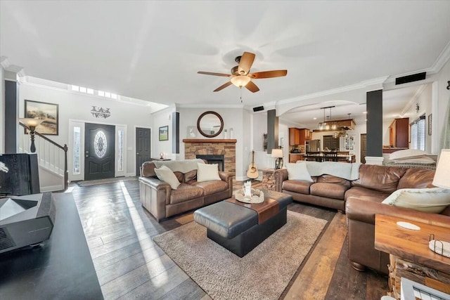 living room featuring ornamental molding, a stone fireplace, dark wood-type flooring, and ceiling fan