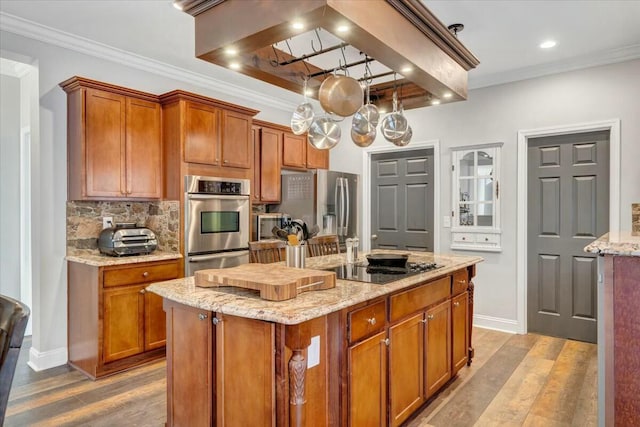 kitchen with appliances with stainless steel finishes, decorative backsplash, a center island, crown molding, and light stone countertops