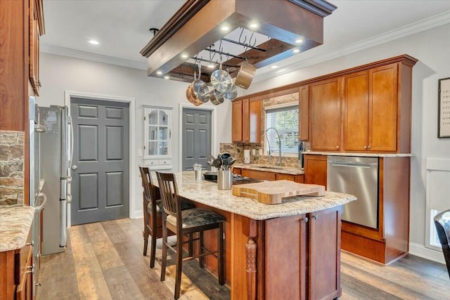 kitchen with sink, crown molding, appliances with stainless steel finishes, light stone countertops, and a kitchen island