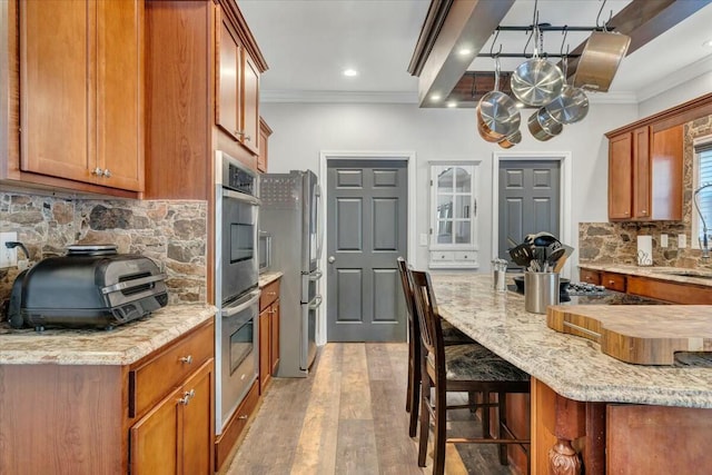 kitchen with light stone counters, light hardwood / wood-style flooring, ornamental molding, and appliances with stainless steel finishes