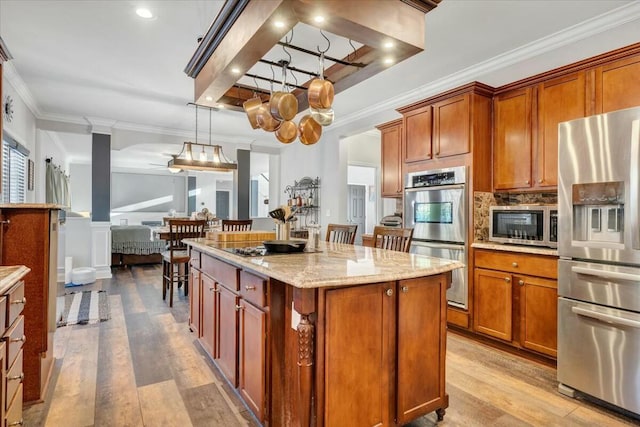 kitchen with a center island, hanging light fixtures, stainless steel appliances, light stone countertops, and decorative columns