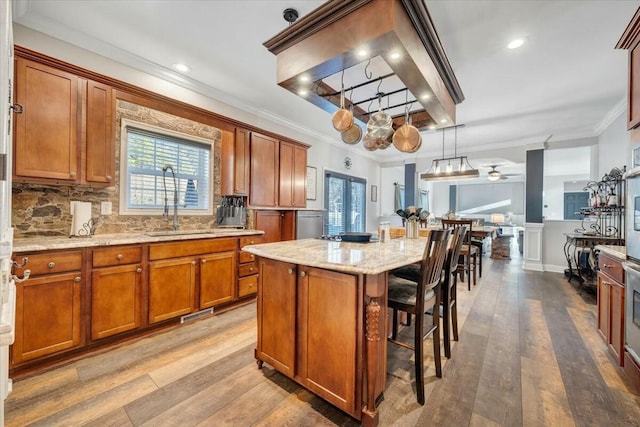 kitchen featuring sink, a breakfast bar area, hanging light fixtures, ornamental molding, and a kitchen island