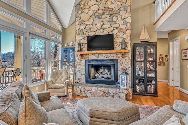 living area with baseboards, a stone fireplace, high vaulted ceiling, and wood finished floors
