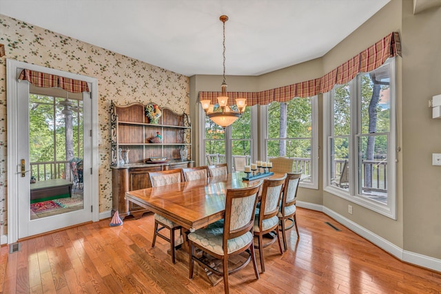 dining space with baseboards, plenty of natural light, light wood finished floors, and a notable chandelier