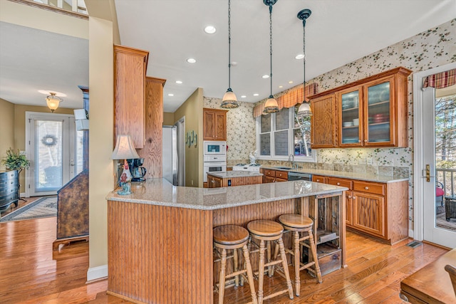kitchen with white appliances, glass insert cabinets, brown cabinetry, and light wood-style flooring