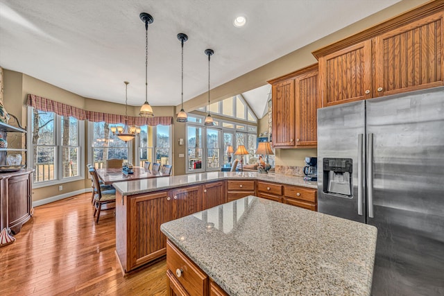 kitchen featuring a peninsula, a healthy amount of sunlight, brown cabinets, stainless steel fridge with ice dispenser, and light stone counters