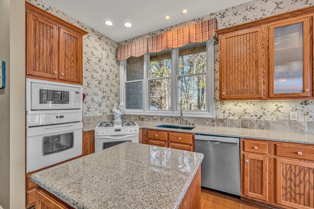 kitchen with a sink, wallpapered walls, white appliances, and light stone countertops