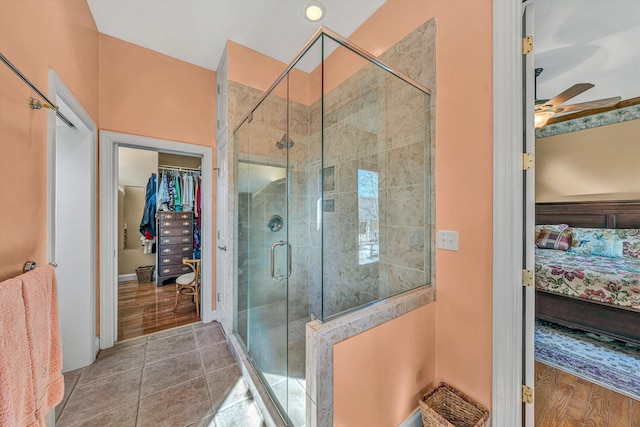 ensuite bathroom with ceiling fan, a shower stall, a walk in closet, and ensuite bath