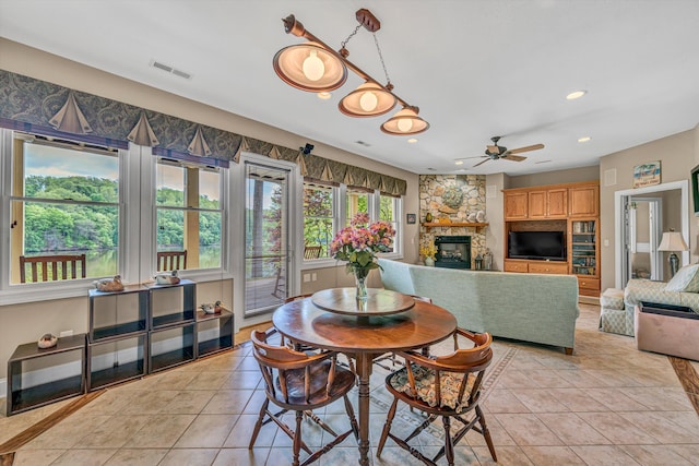 dining space with light tile patterned floors, ceiling fan, a fireplace, and visible vents