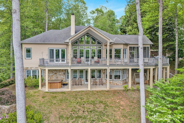 back of house with a wooden deck, stone siding, a chimney, a patio area, and a hot tub