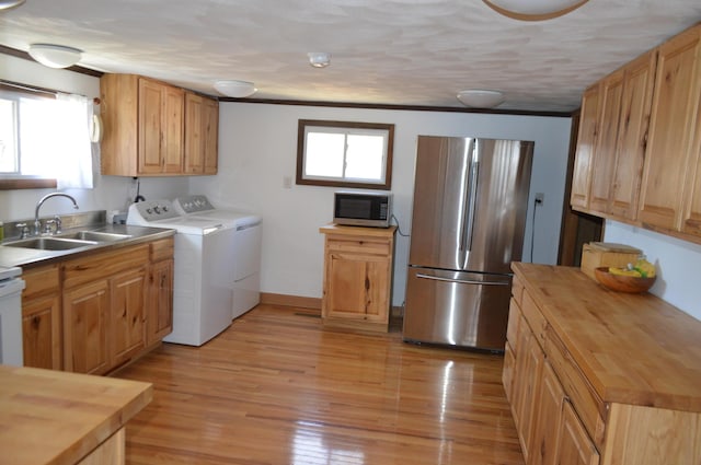 kitchen featuring light wood finished floors, washer and clothes dryer, stainless steel appliances, a healthy amount of sunlight, and a sink