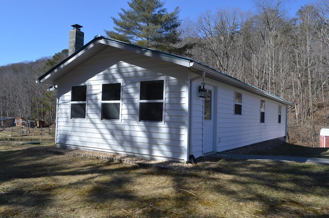 view of property exterior with a yard, a chimney, and a view of trees