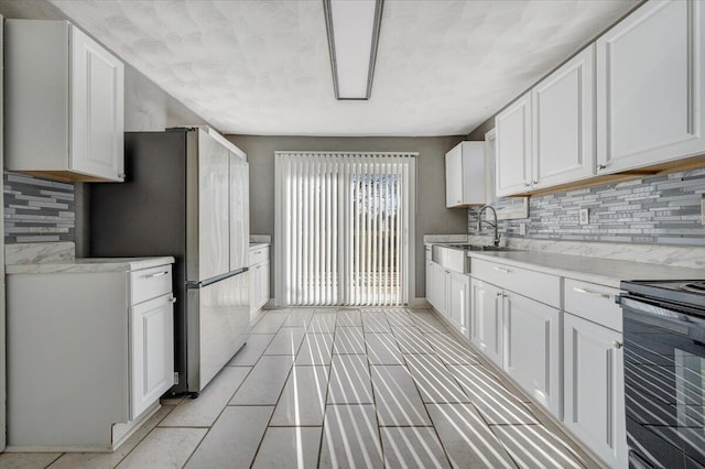 kitchen featuring sink, white cabinetry, black / electric stove, stainless steel fridge, and backsplash