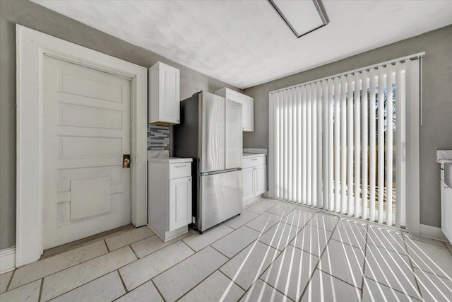 kitchen with white cabinetry, backsplash, and stainless steel refrigerator