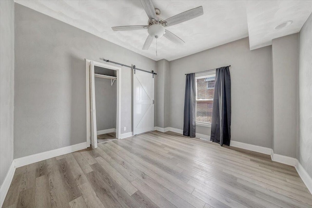 unfurnished bedroom featuring a closet, a barn door, ceiling fan, and light hardwood / wood-style flooring