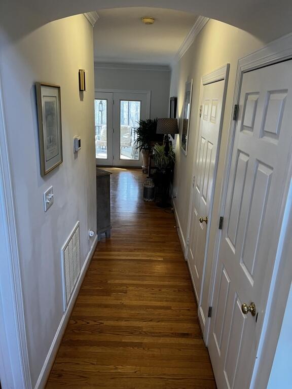 hall with dark wood-style floors, ornamental molding, visible vents, and baseboards